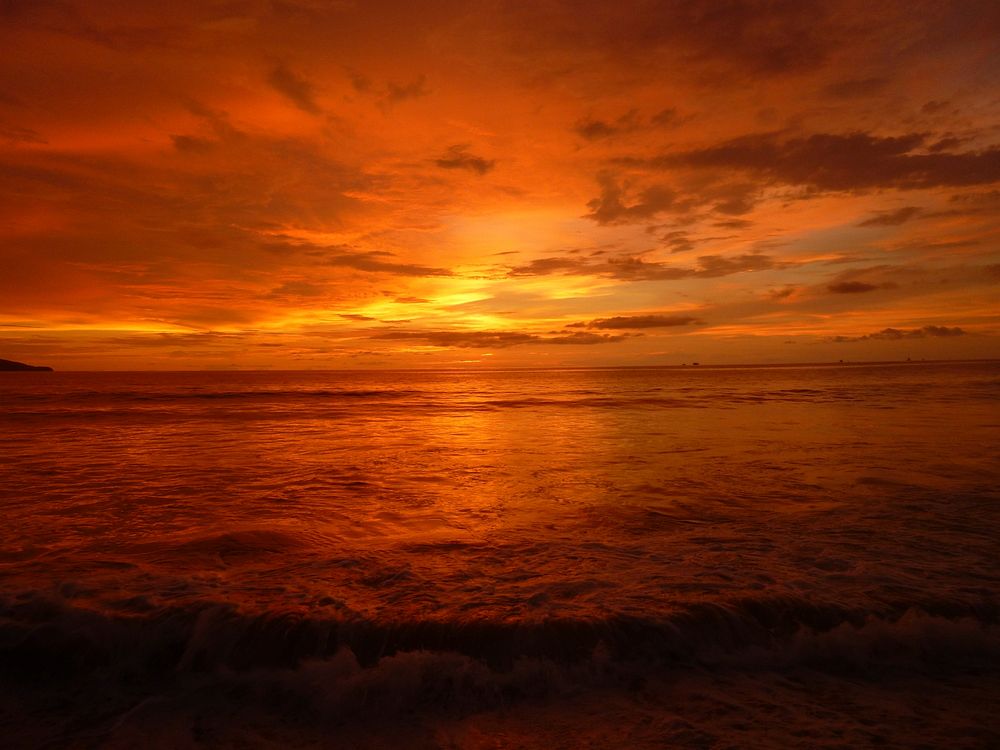 Dramatic deep orange sunset over the ocean with golden and grey wispy clouds in the sky.. Original public domain image from…
