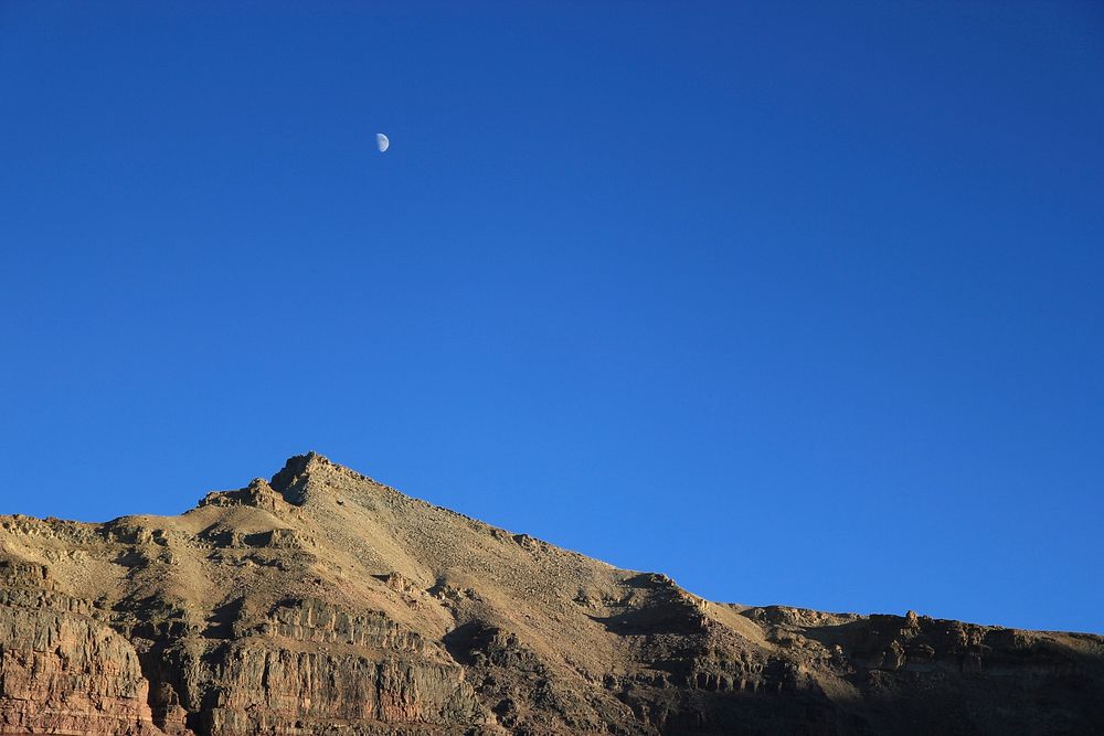 Half moon on a blue sky over a rocky ridge. Original public domain image from Wikimedia Commons