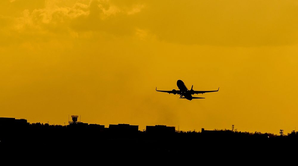 A silhouette of an airplane against an orange sky over an airport. Original public domain image from Wikimedia Commons