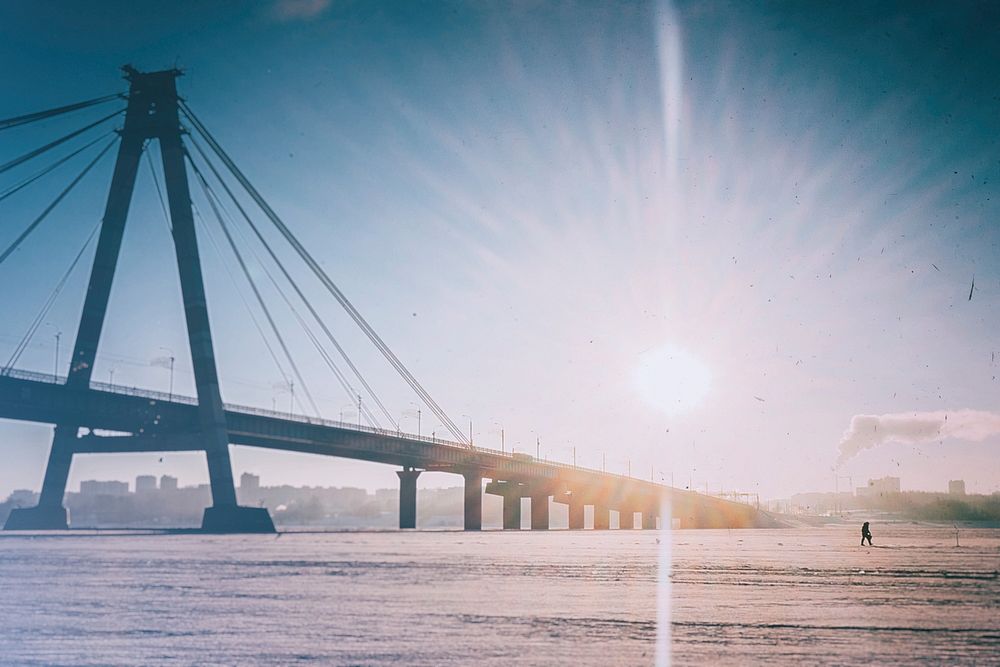 A by the sun illuminated bridge in Cherepovets spans over ice during winter a winter day. Original public domain image from…