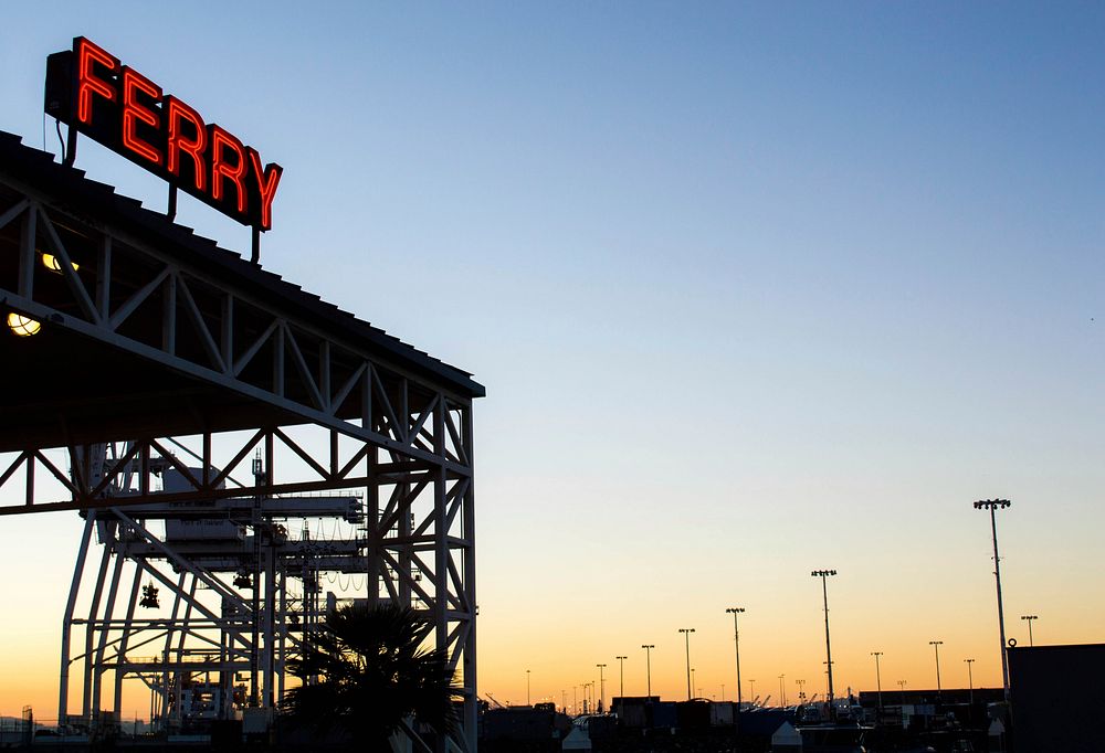 Neon "ferry" sign glows over an industrial structure at sunset. Original public domain image from Wikimedia Commons