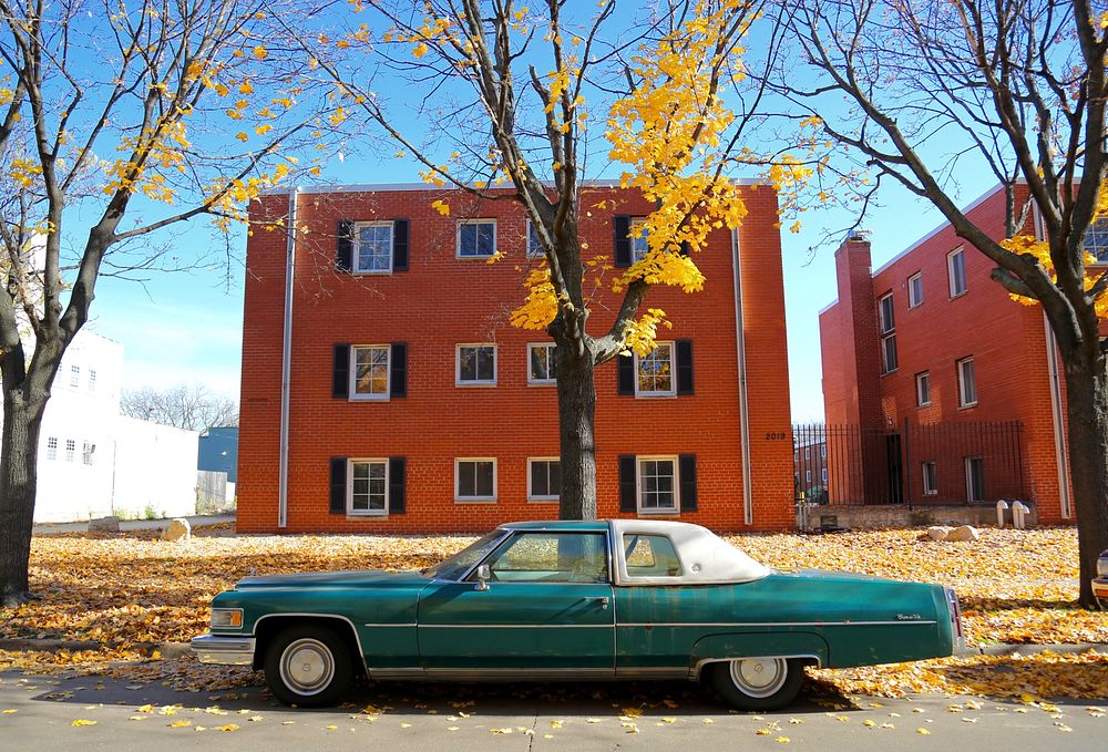 Vintage cyan car parked on a street in front of a brick building in autumn. Original public domain image from Wikimedia…