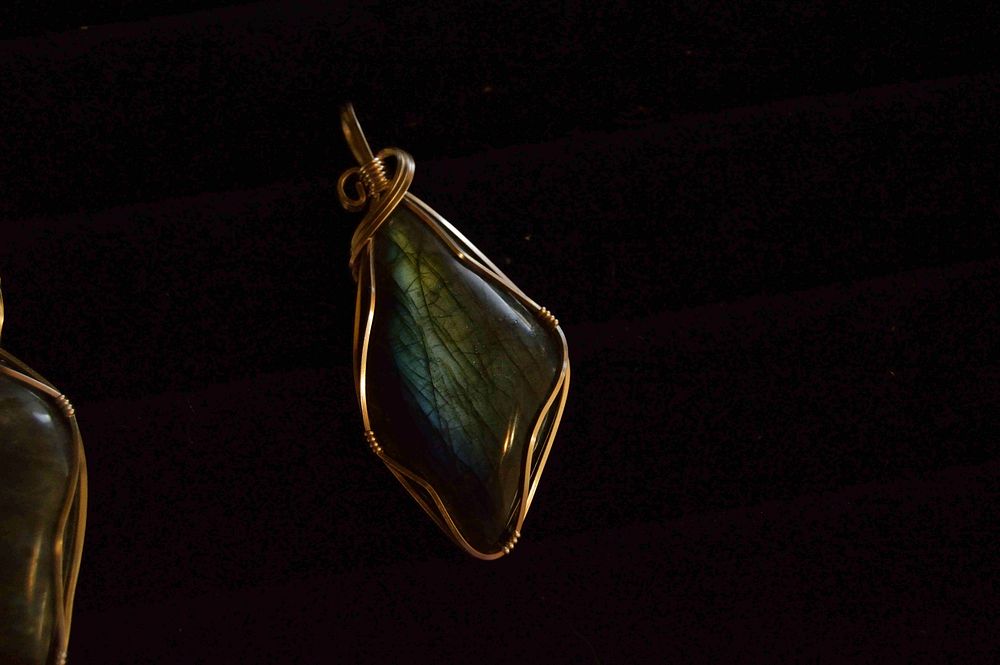 A gemstone pendant wrapped in a copper wire against a black background. Original public domain image from Wikimedia Commons