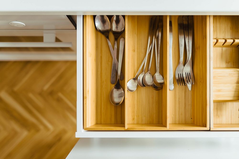 View from above of wooden utensil drawer above wooden floor in kitchen with white cabinets. Original public domain image…