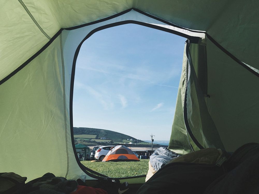 The view of a campsite and clear blue sky from inside of a green tent. Original public domain image from Wikimedia Commons