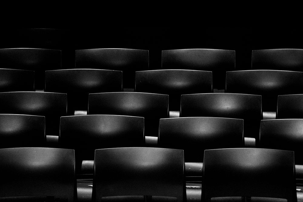 A dim shot of rows of empty seats in a movie theater. Original public domain image from Wikimedia Commons