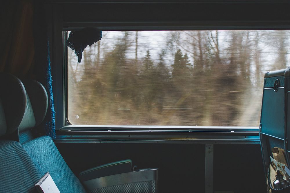 The interior of a moving train with empty seats next to a window. Original public domain image from Wikimedia Commons