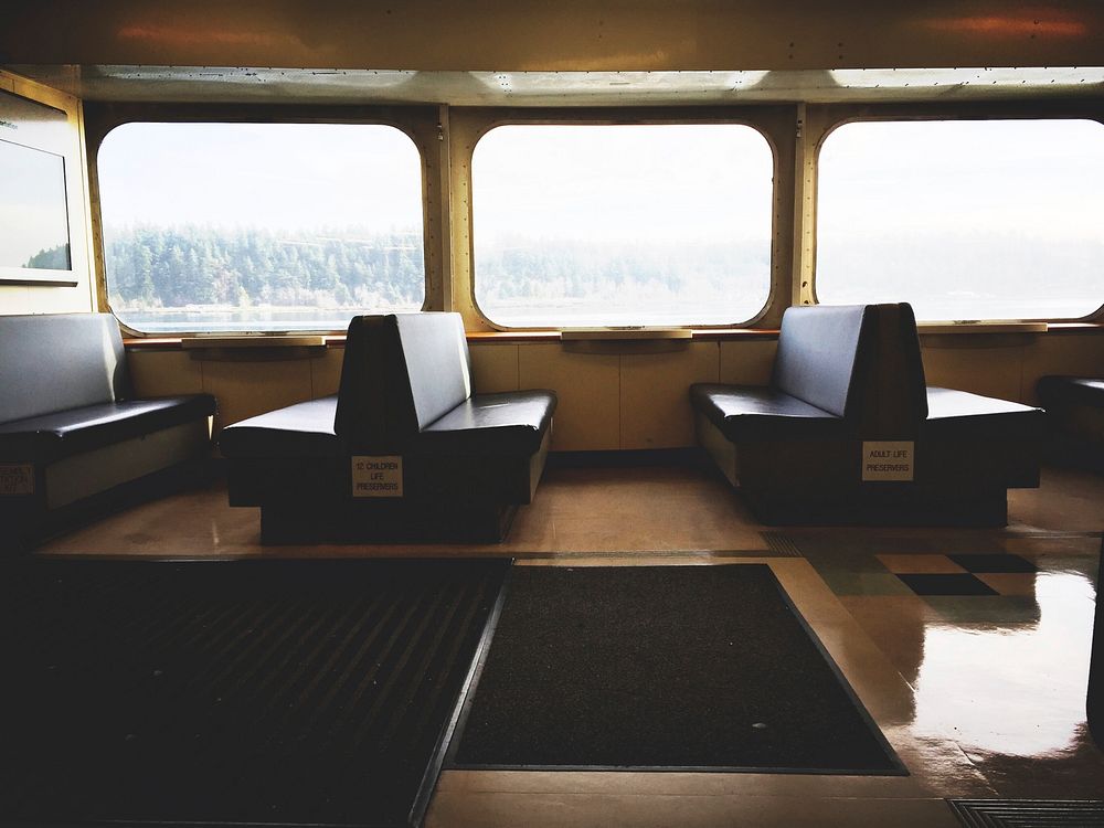 Interior of ferry with empty seats, dark mats, and a view of trees out the window. Original public domain image from…