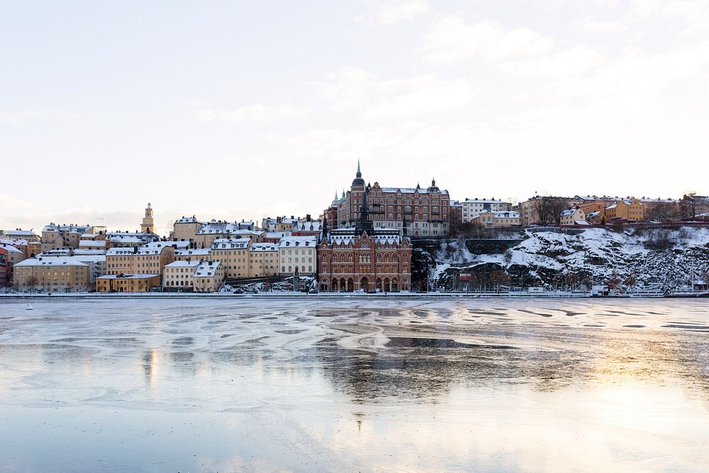 A Swedish city with tan and brown buildings by the shore of a frozen lake. Original public domain image from Wikimedia…