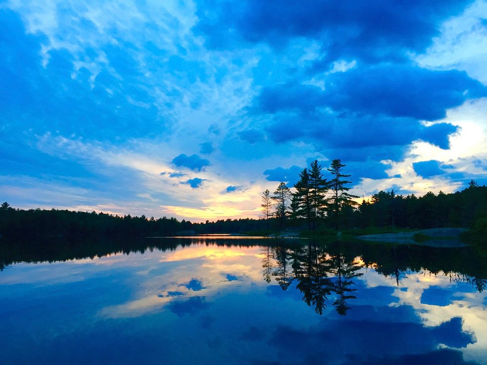 A bright blue cloudy sky and its reflection in a lake at Kawartha Highlands Provincial Park. Original public domain image…