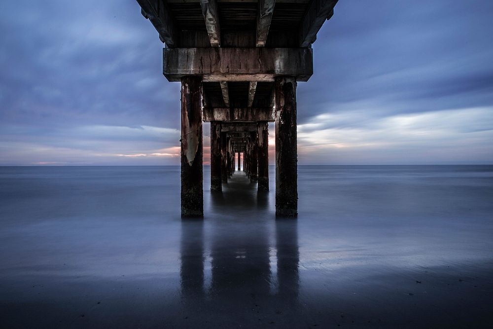 View into the distance under the pier between the pillars at Saint Augustine Beach. Original public domain image from…