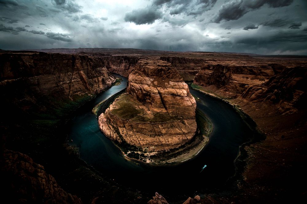A dim shot of a horseshoe-shaped river bend in a canyon under a stormy sky. Original public domain image from Wikimedia…