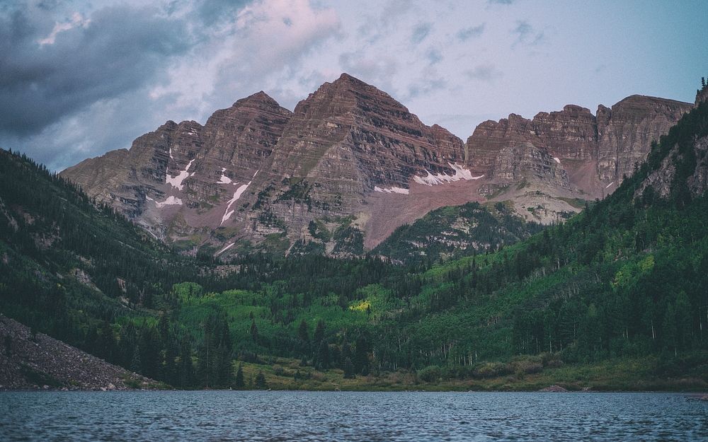Two red-hued mountain peaks towering above a green forest and a lake in Maroon Bells. Original public domain image from…