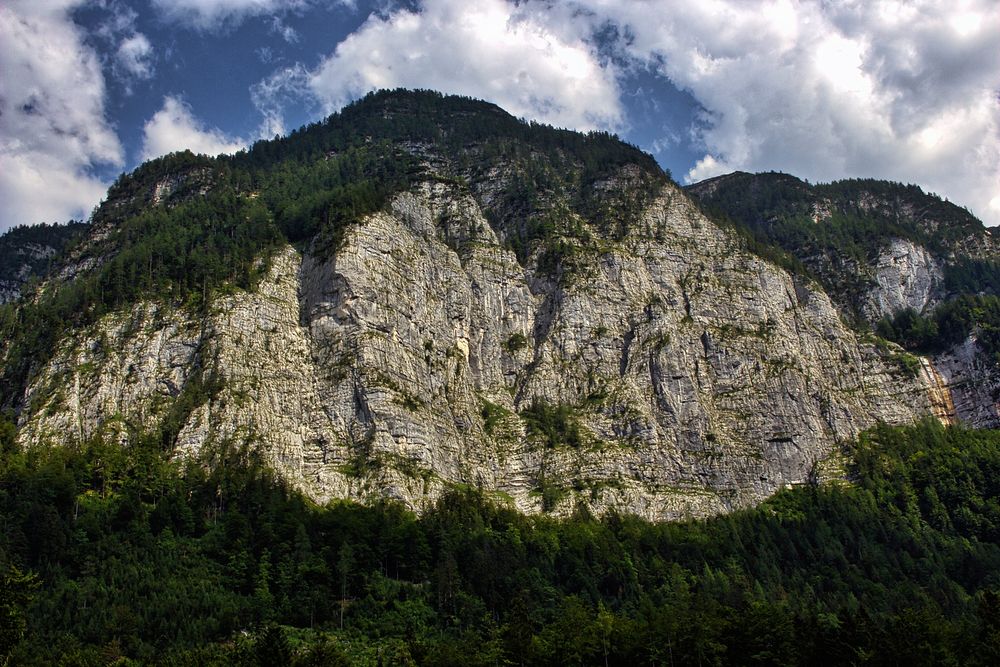 A steep rugged mountain with green woods on its top. Original public domain image from Wikimedia Commons