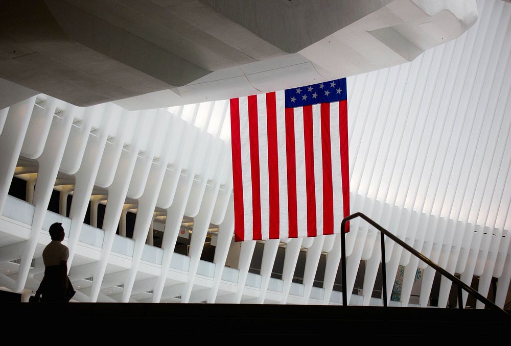 An American flag hands off a balcony inside a modern building. Original public domain image from Wikimedia Commons