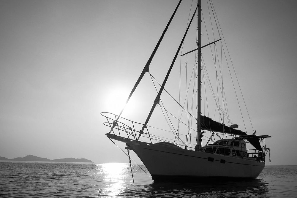 Black and white shot of yacht on sea with clear sky and sun in background. Original public domain image from Wikimedia…