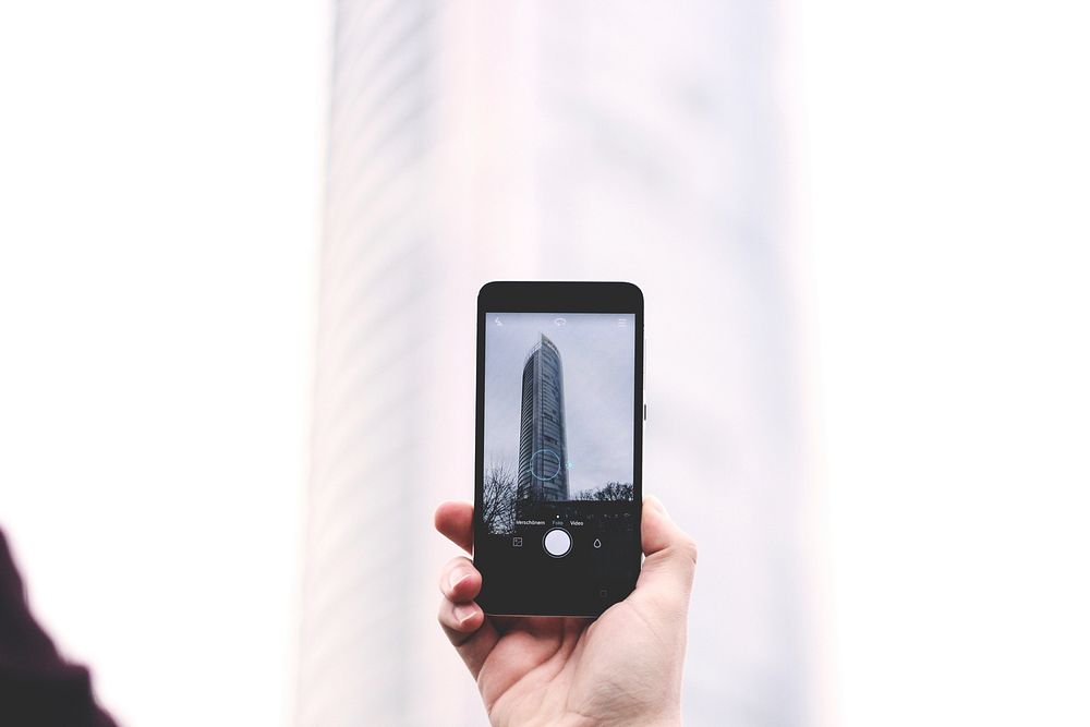 A person taking a picture of a skyscraper with a phone. Original public domain image from Wikimedia Commons