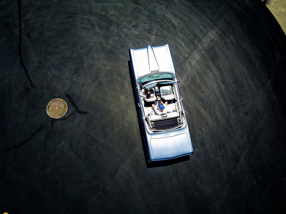 Drone view of blue classic convertible car driving on black surface in the sun. Original public domain image from Wikimedia…