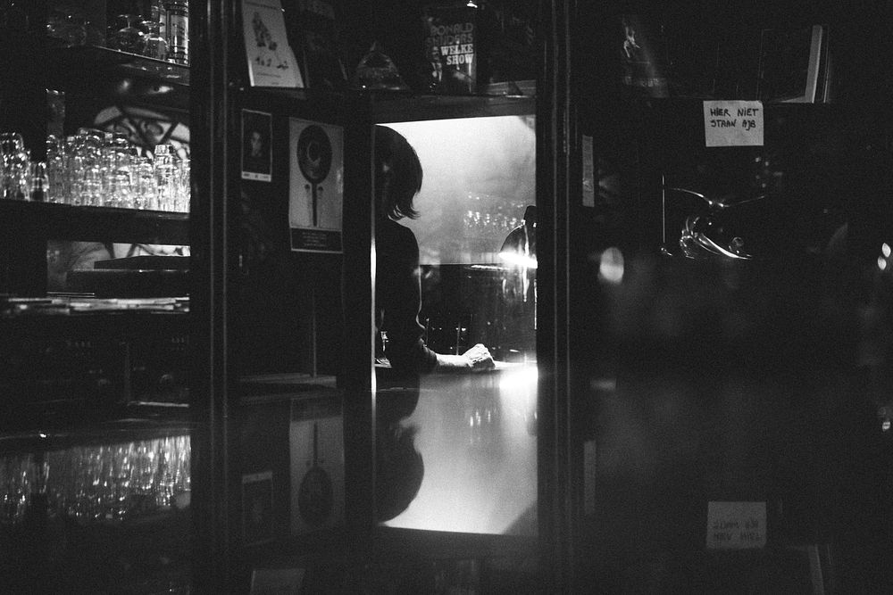 A black-and-white shot of a bar and a female cashier in Amsterdam.. Original public domain image from Wikimedia Commons