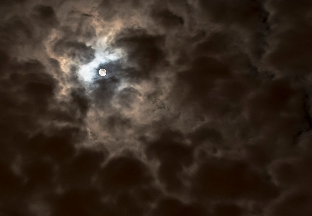 A full moon peeking through a cloudy night sky.Original public domain image from Wikimedia Commons