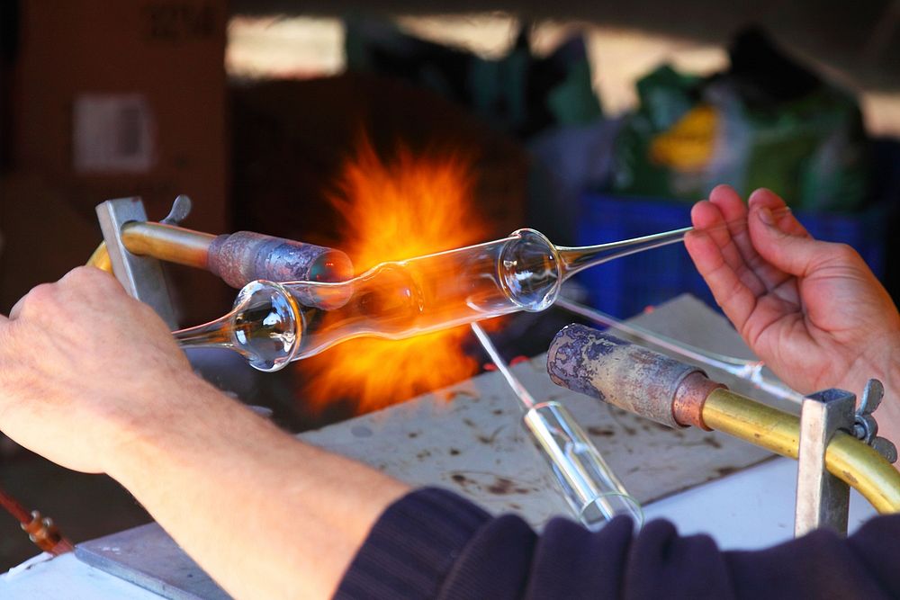 A glassblower pulls and blows a glass with heat. Original public domain image from Wikimedia Commons