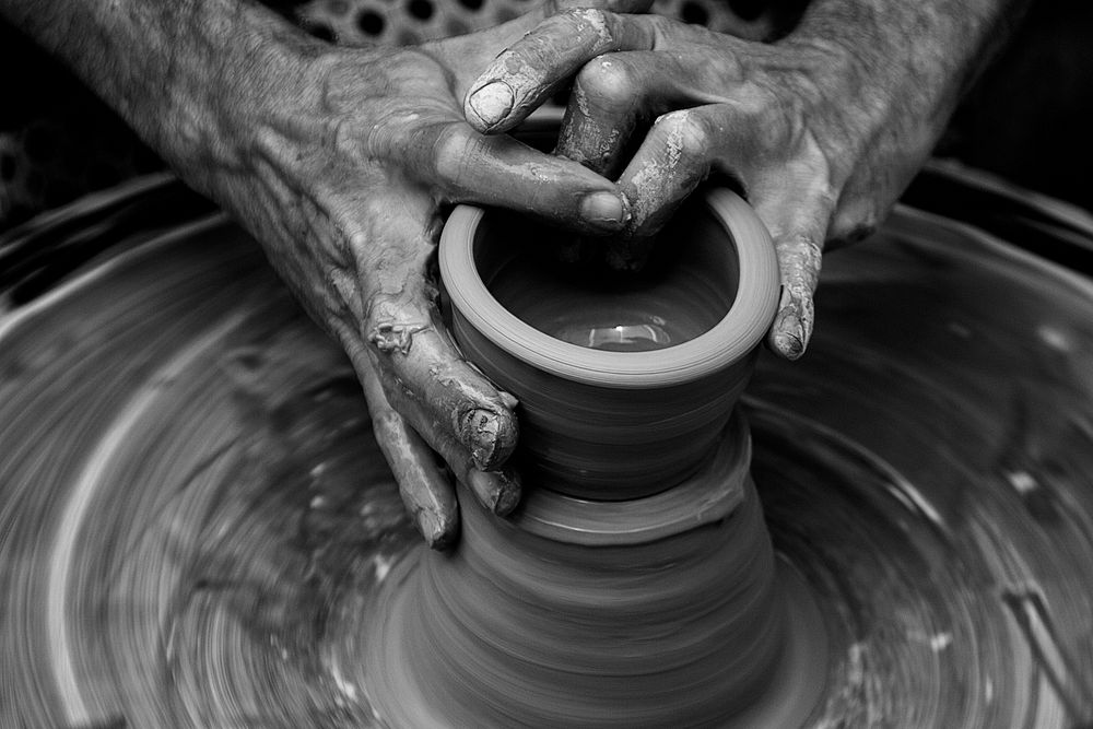 Messy hands sculpting on a pottery wheel in motion. Original public domain image from Wikimedia Commons