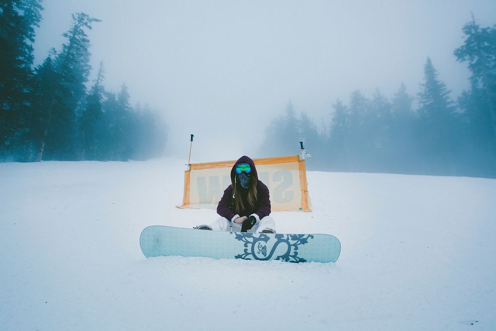 A man sitting with his snowboard at thes starting point on a ski hill. Original public domain image from Wikimedia Commons