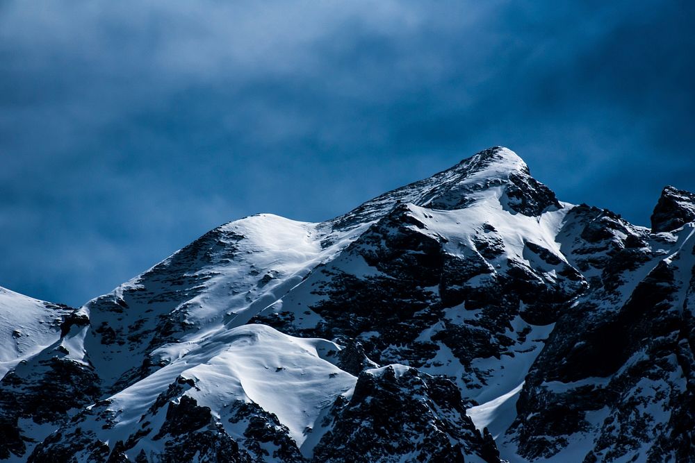 Snow covers the summit of a mountain ridge in a blue landscape. Original public domain image from Wikimedia Commons