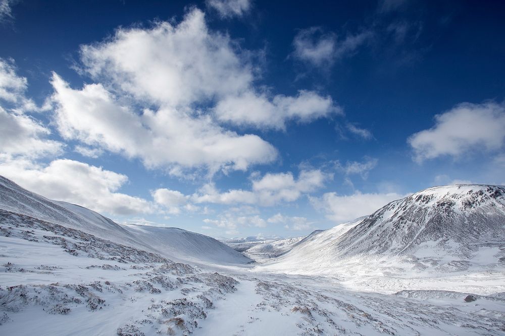 A snow filled valley in between mountains and a cloudy, blue sky in Cairngorms National Park in Scotland. Original public…