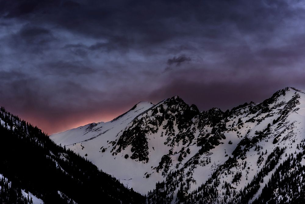 A snow-capped mountain ridge under dark gray evening sky. Original public domain image from Wikimedia Commons
