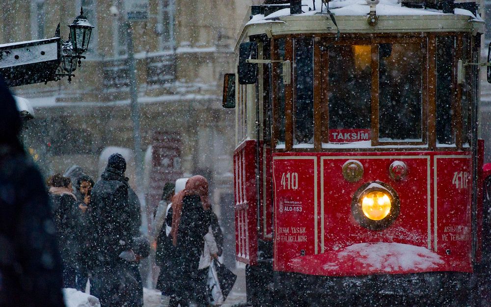 A red trolley picks up passengers in winter clothing during snowfall. Original public domain image from Wikimedia Commons