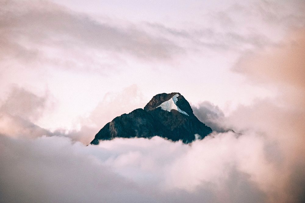 A granite mountain peak rising up above pink-hued clouds. Original public domain image from Wikimedia Commons