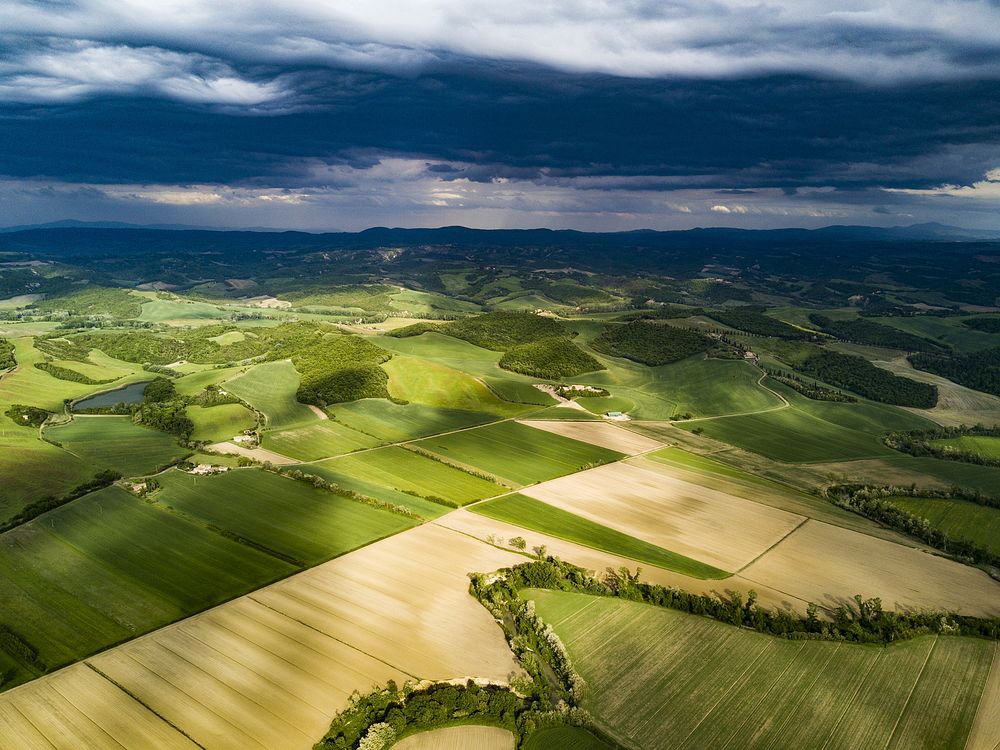 A drone shot of a patchwork of green fields in Tuscany. Original public domain image from Wikimedia Commons