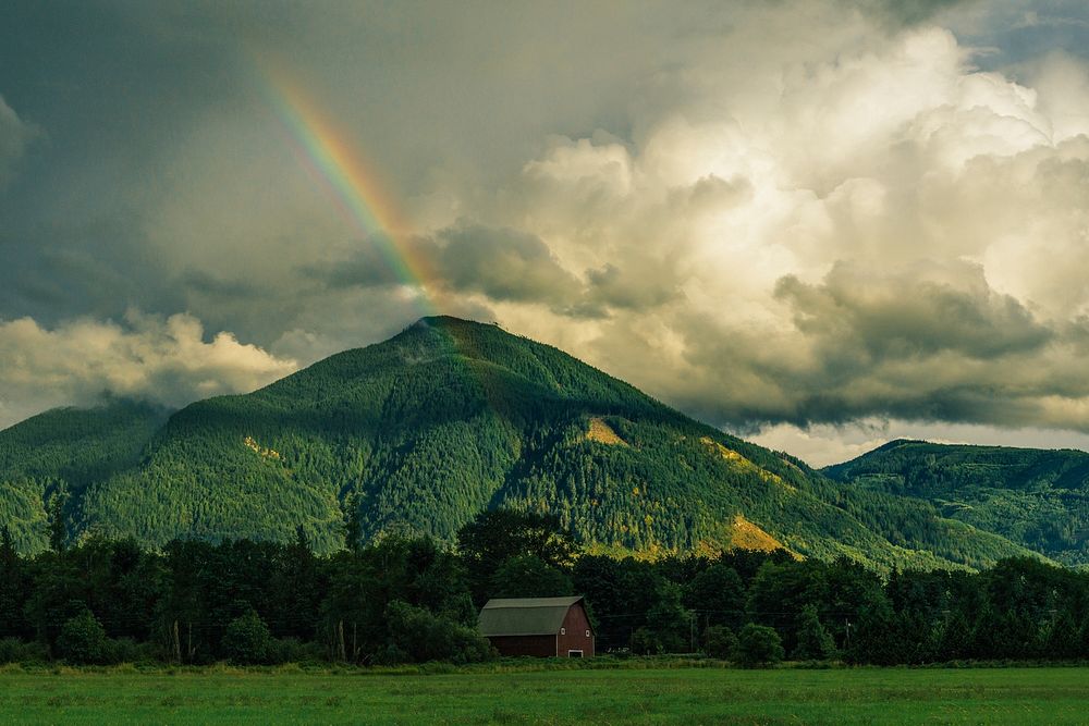 A rainbow over a barn near a wooded mountain. Original public domain image from Wikimedia Commons
