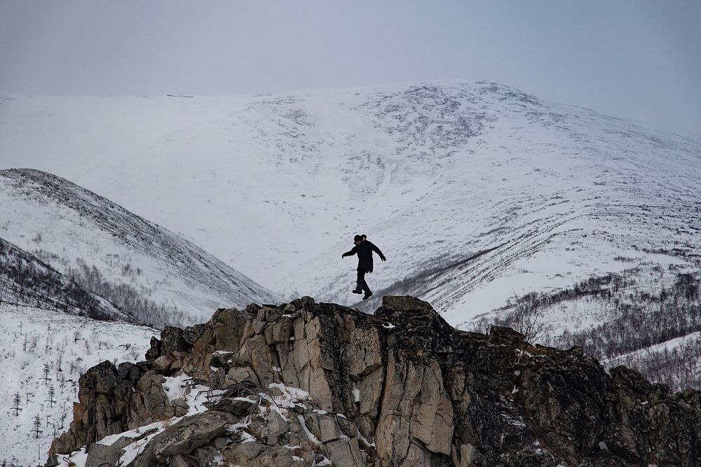 Person jumping on rocks on cliffs covered in snow. Original public domain image from Wikimedia Commons