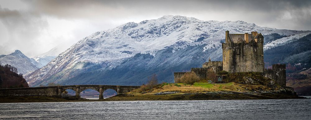 A castle on an island in Scotland with a bridge and a mountain in the background. Original public domain image from…