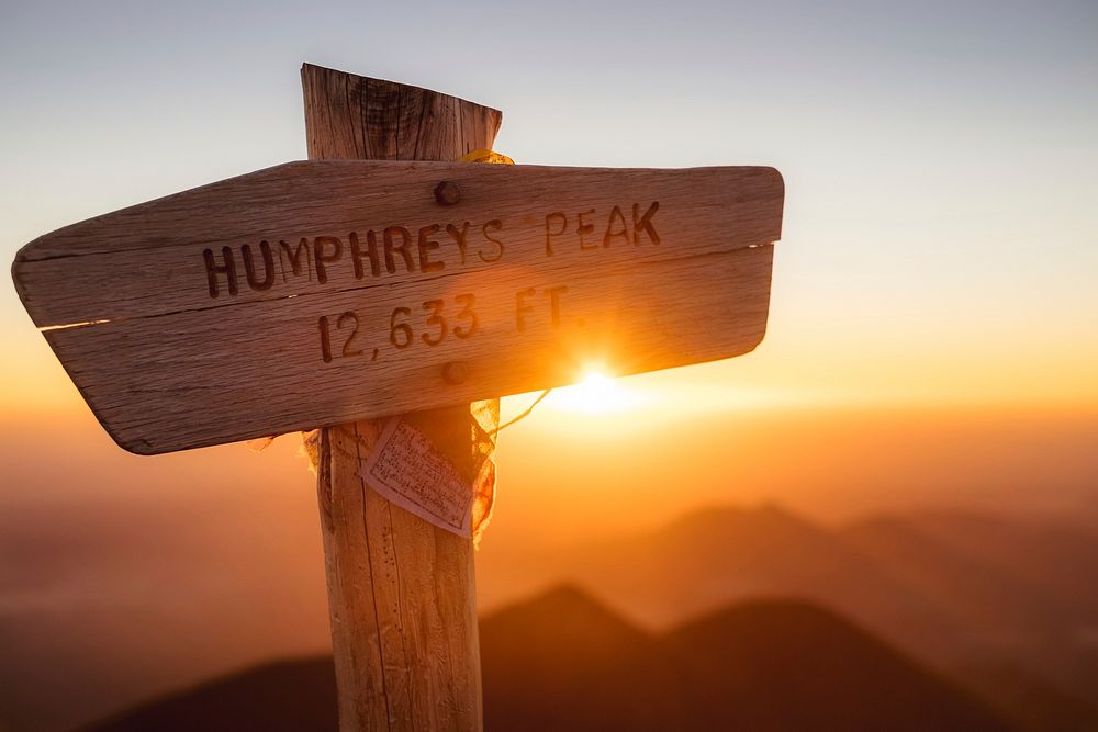 A wooden signpost reading “Humphreys Peak 12,633 ft” during sunrise. Original public domain image from Wikimedia Commons