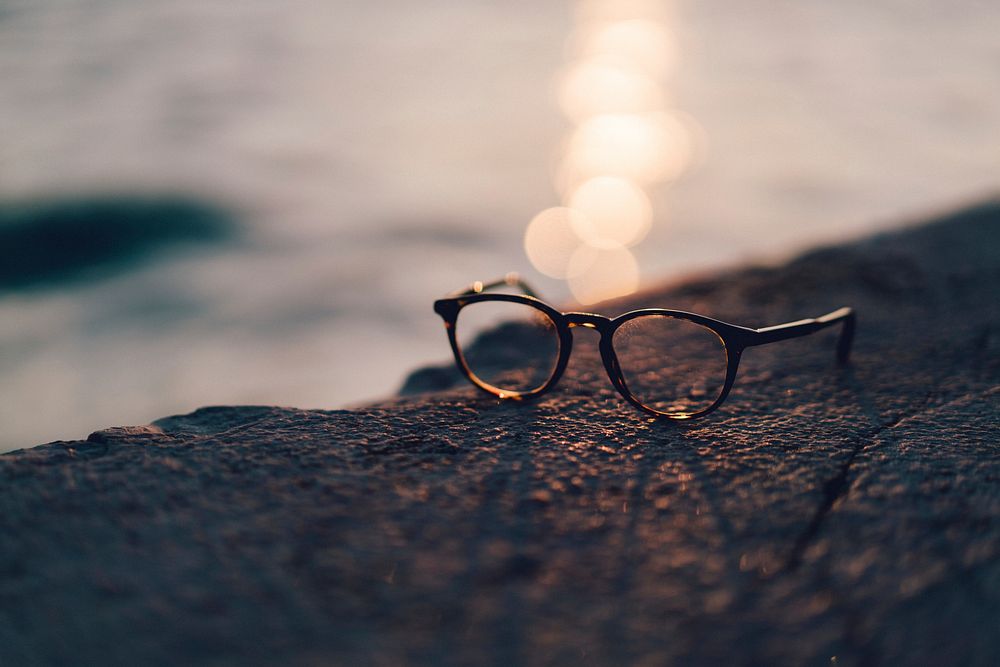 A pair of glasses sits on a rocky surface by a body of water. Original public domain image from Wikimedia Commons