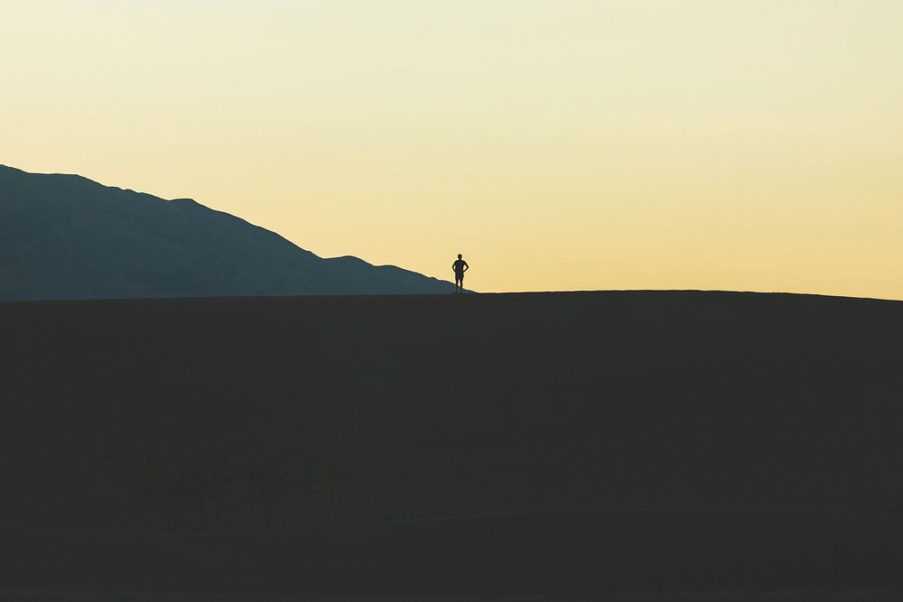 A person's silhoutte against the orange sky on a sand dune at Death Valley National Park. Original public domain image from…