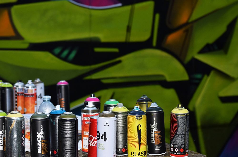 Set of varied spray cans in front of green graffiti mural at International Graffiti Festival 2017. Original public domain…