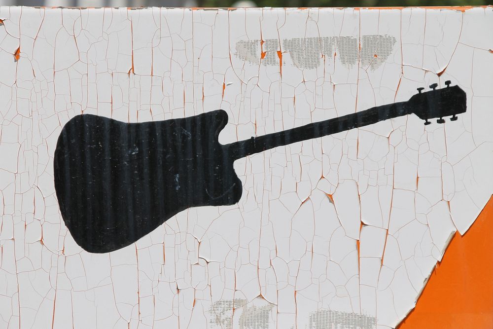 A black guitar on a white background painted on an old wooden fence. Original public domain image from Wikimedia Commons