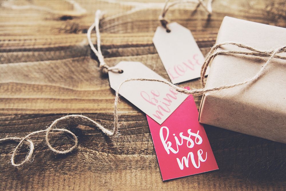 Paper tags with “kiss me” written on one of them next to a wrapped gift. Original public domain image from Wikimedia Commons