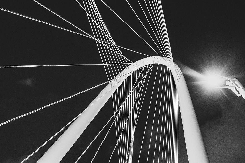 Black and white shot of bridge architecture with metal wire from below with light. Original public domain image from…