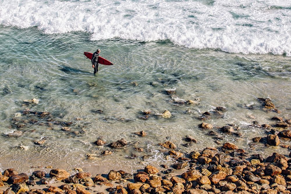 Surfer with a surfboard standing in the shallow ocean water at Point Dume State Beach. Original public domain image from…