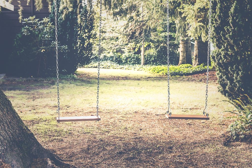 A child's swingset in a playground in a garden. Original public domain image from Wikimedia Commons