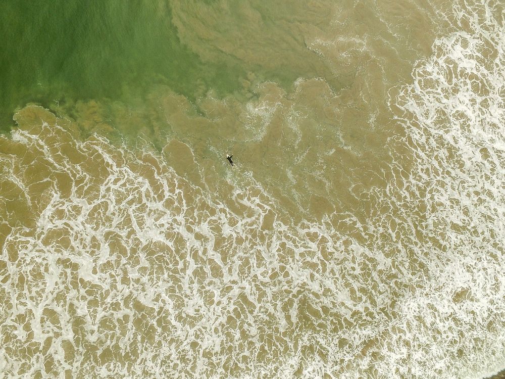 An overhead drone shot of a surfer in a foaming ocean at San Clemente. Original public domain image from Wikimedia Commons