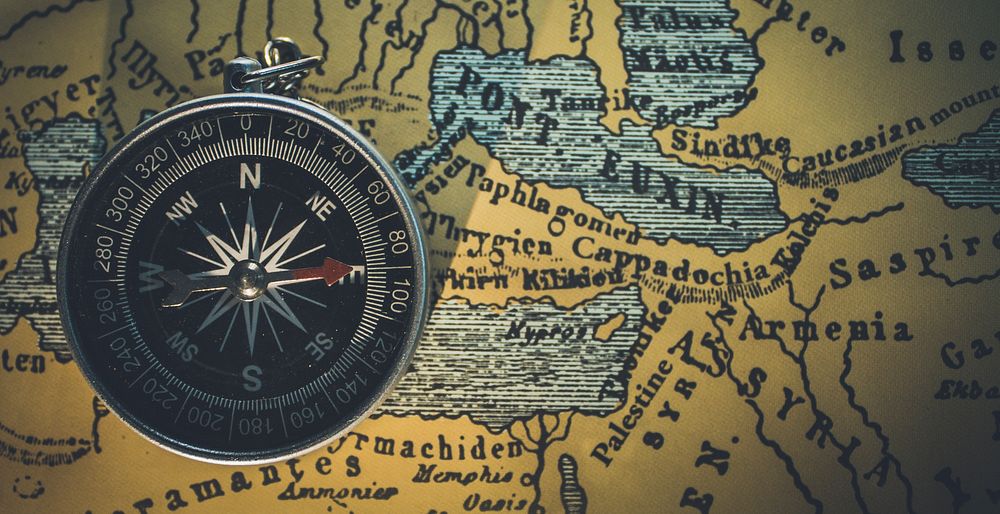 An overhead shot of a compass laid out on an old map. Original public domain image from Wikimedia Commons