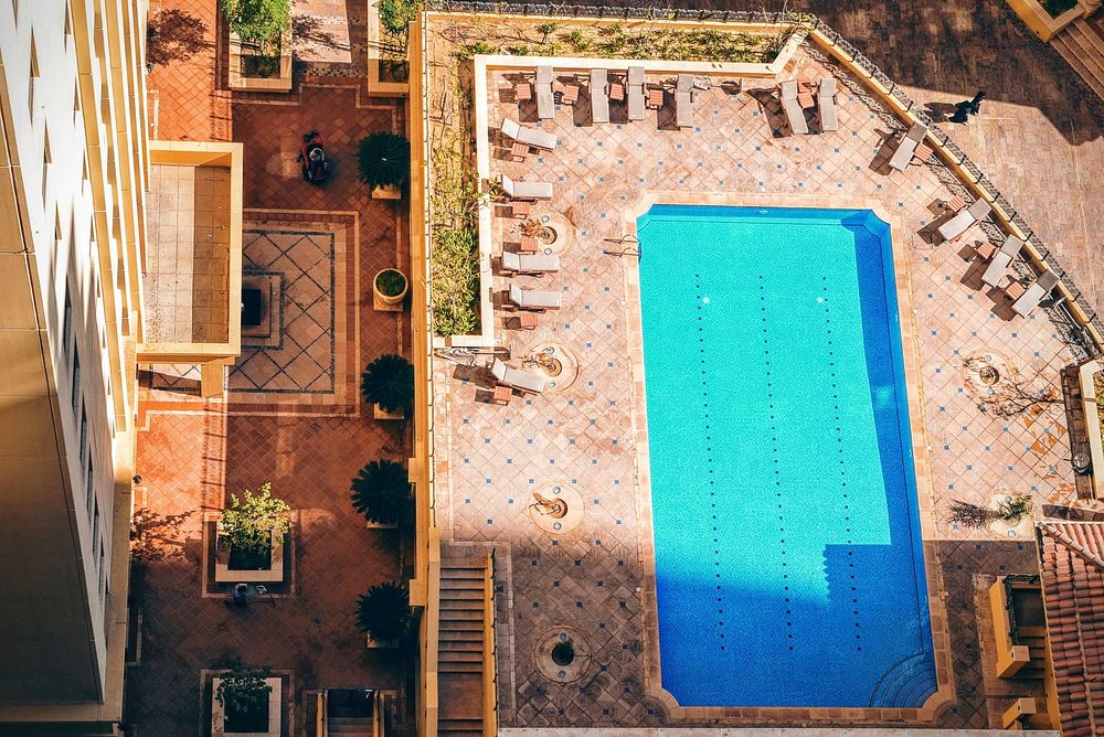 Drone view of pool near building surrounded by lounger deck chairs. Original public domain image from Wikimedia Commons