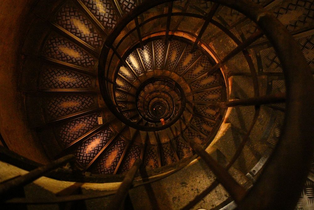 A worn spiral staircase with dark wood and faded designs. Original public domain image from Wikimedia Commons