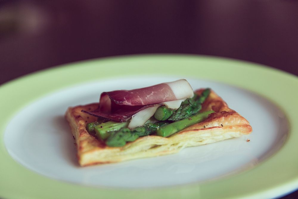 Slice of pancetta and asparagus on a square of puff pastry laid on a clean white plate. Original public domain image from…